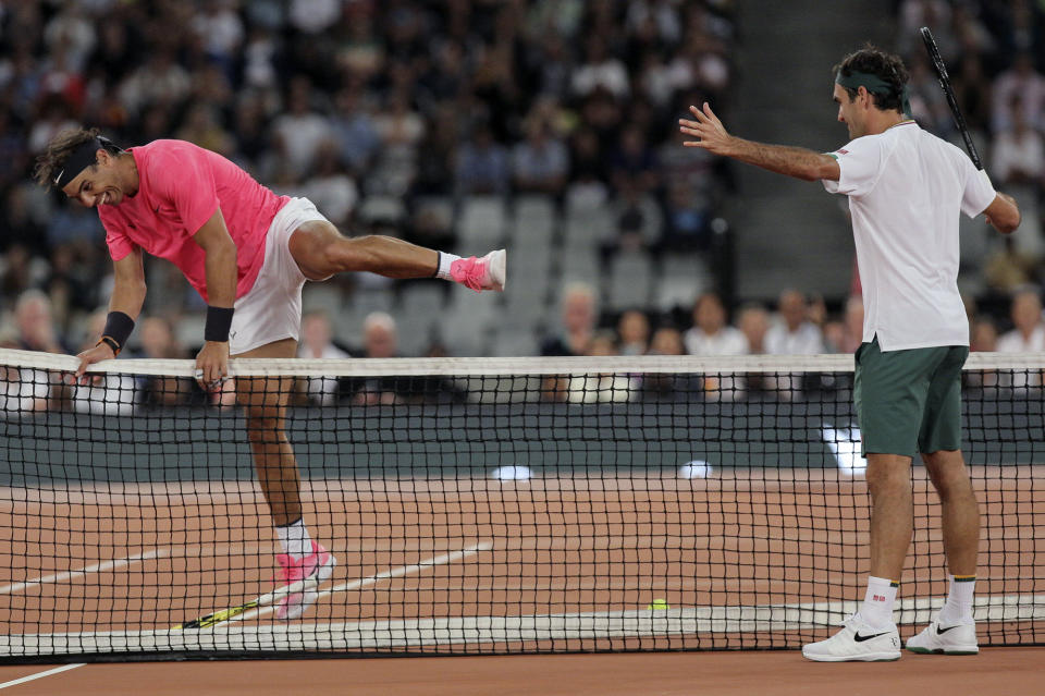 Rafael Nadal, left, jumps the net while Roger Federer watches on during their exhibition tennis match held at the Cape Town Stadium in Cape Town, South Africa, Friday Feb. 7, 2020. (AP Photo/Halden Krog)