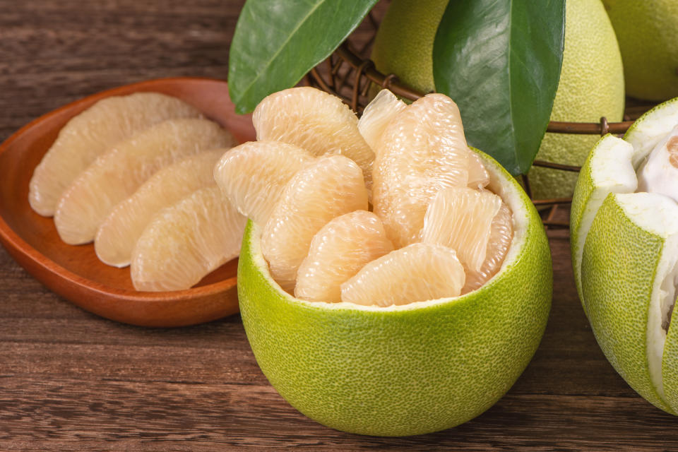 Fresh peeled pomelo, grapefruit, shaddock with green leaves on dark wooden plank table. Seasonal fruit near mid-autumn festival, close up, copy space