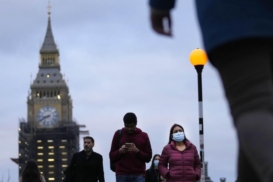 People partly wearing a face covering walk across Westminster Bridge in London, Wednesday, Dec. 15, 2021. As of Monday in England, people were urged to work from home if possible, with long lines forming at vaccination centers for people to get booster shots to protect themselves against the coronavirus omicron variant. (AP Photo/Frank Augstein)