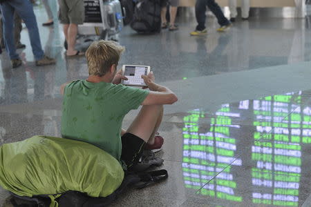 The departure board is reflected on the floor as a passenger sits in the international terminal at Ngurah Rai Airport on the Indonesian resort island of Bali July 10, 2015 in this photo taken by Antara Foto. REUTERS/Nyoman Budhiana/Antara Foto