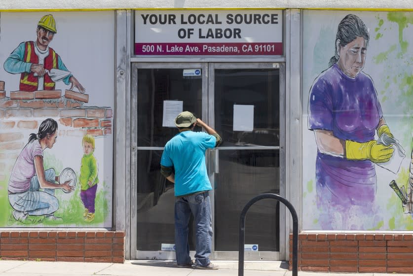 A worker looks inside the closed doors of the Pasadena Community Job Center in Pasadena, Calif., Thursday, May 7, 2020, during the coronavirus outbreak. The center normally connects members of the community, residential customers and small business owners with skilled day laborers. (AP Photo/Damian Dovarganes)