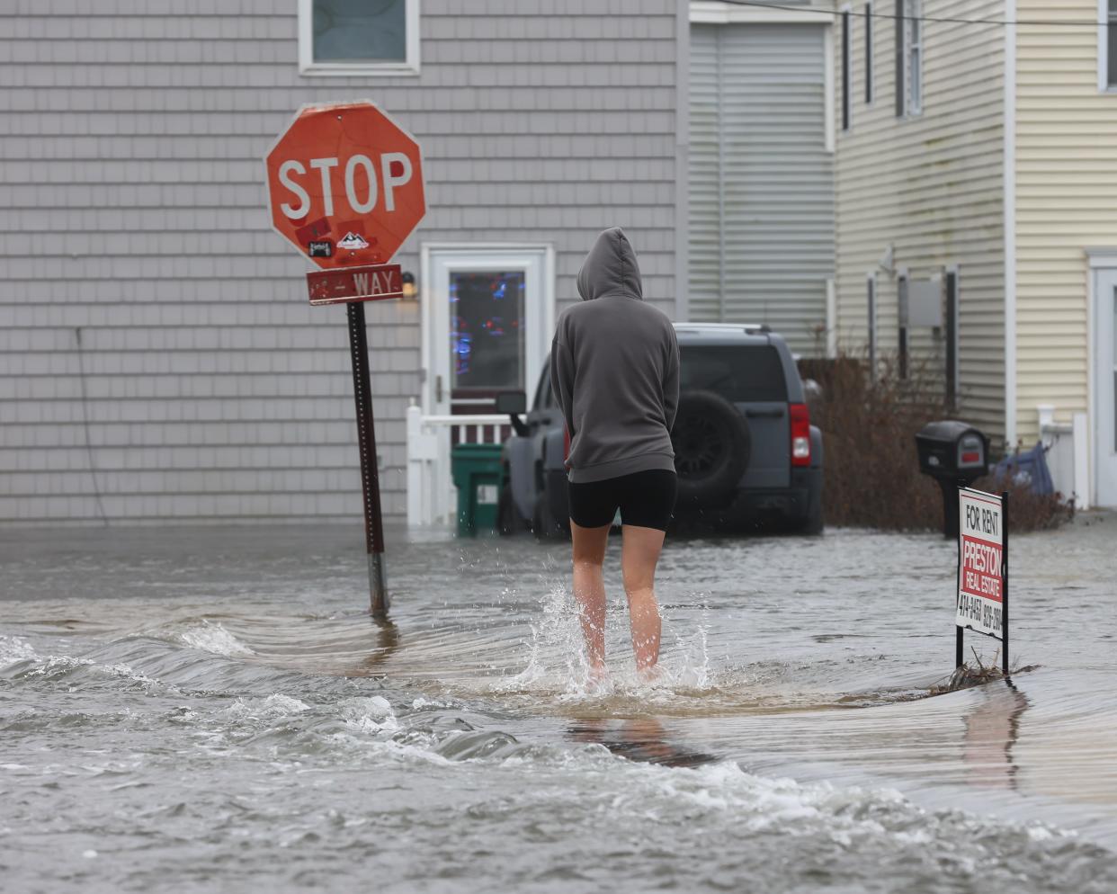 A Hampton Beach resident makes her way back to her house while wading in shorts and bare feet through the high tide on Brown Avenue at Hampton Beach on Saturday, Jan. 13, 2024.