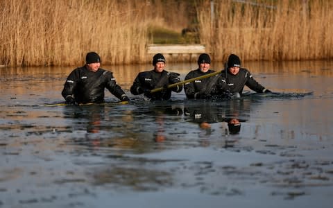 Four officers wade through the waist-deep water, using sticks to break the ice and search beneath the surface - Credit: SWNS