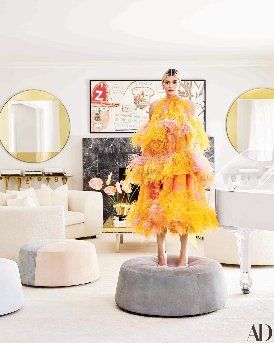Kylie Jenner, in a Marc Jacobs dress and Christian Louboutin heels, stands in front of a Jean-Michel Basquiat artwork in her living room.
