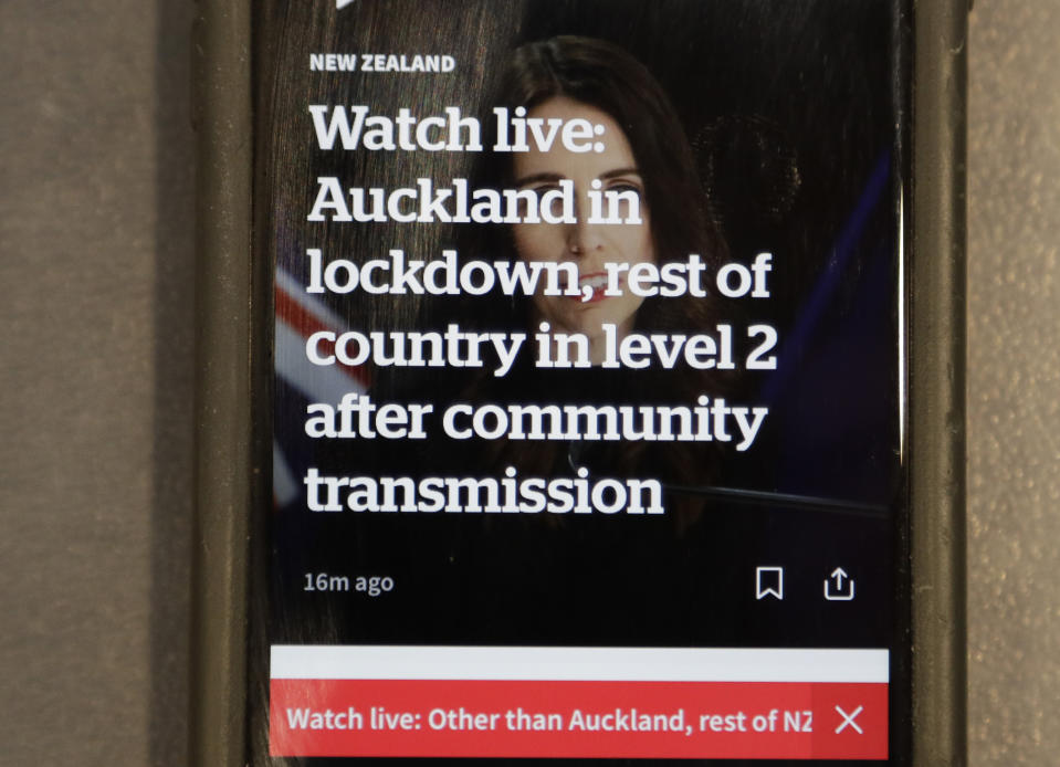 A news alert is displayed on a mobile phone in Christchurch, New Zealand, Tuesday, Aug. 11, 2020. New Zealand Prime Minister Jacinda Ardern said Tuesday that authorities have found four cases of the coronavirus in one Auckland household from an unknown source, the first cases of local transmission in the country in 102 days. (AP Photo/Mark Baker)