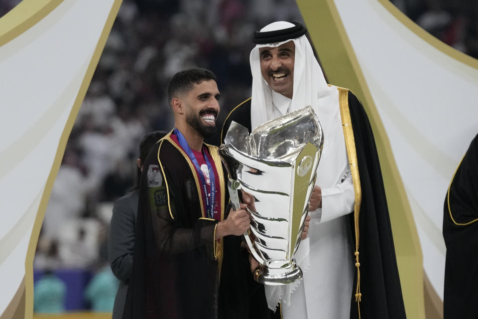 Qatar's Hasan Al Haydos, left, is presented the trophy by Emir of Qatar Tamim bin Hamad Al Thani, after Qatar won the Asian Cup final soccer match between Qatar and Jordan at the Lusail Stadium in Lusail, Qatar, Saturday, Feb. 10, 2024. Qatar won 3-1. (AP Photo/Aijaz Rahi)