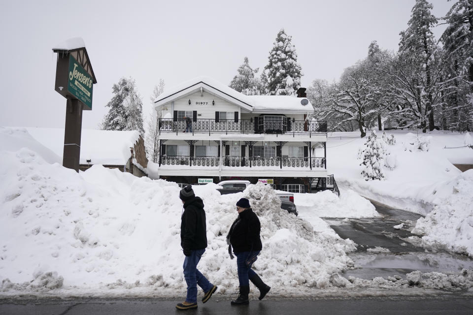 Two residents walk past the piles of snow in Running Springs, Calif., Tuesday, Feb. 28, 2023. Beleaguered Californians got hit again Tuesday as a new winter storm moved into the already drenched and snow-plastered state, with blizzard warnings blanketing the Sierra Nevada and forecasters warning residents that any travel was dangerous. (AP Photo/Jae C. Hong)