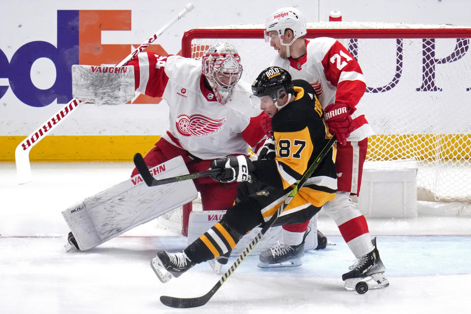 Detroit Red Wings' Austin Czarnik (21) hauls down Pittsburgh Penguins' Sidney Crosby (87) in front of goaltender Alex Lyon during the first period of an NHL hockey game in Pittsburgh, Sunday, March 17, 2024. Czarnik drew a two-minute minor penalty on the play. (AP Photo/Gene J. Puskar)