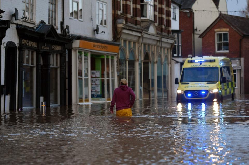 A man wades through flood water towards an ambulance in a flooded street in Tenbury Wells (AFP via Getty Images)