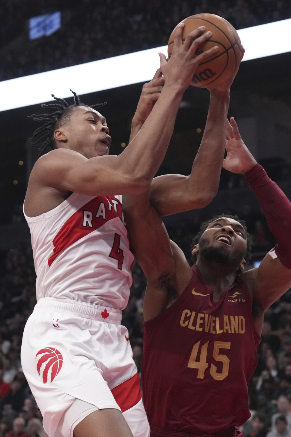 Toronto Raptors' Scottie Barnes (4) battles for an offensive rebound with Cleveland Cavaliers Donovan Mitchell (45) during the first half of an NBA basketball game in Toronto, Monday, Jan. 1, 2024. (Chris Young/The Canadian Press via AP)