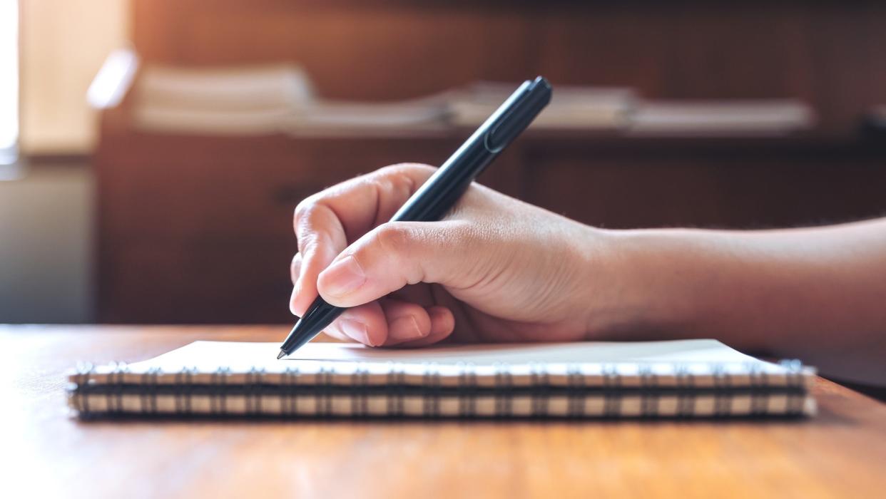 Closeup image of a hand writing down on a white blank notebook on wooden table