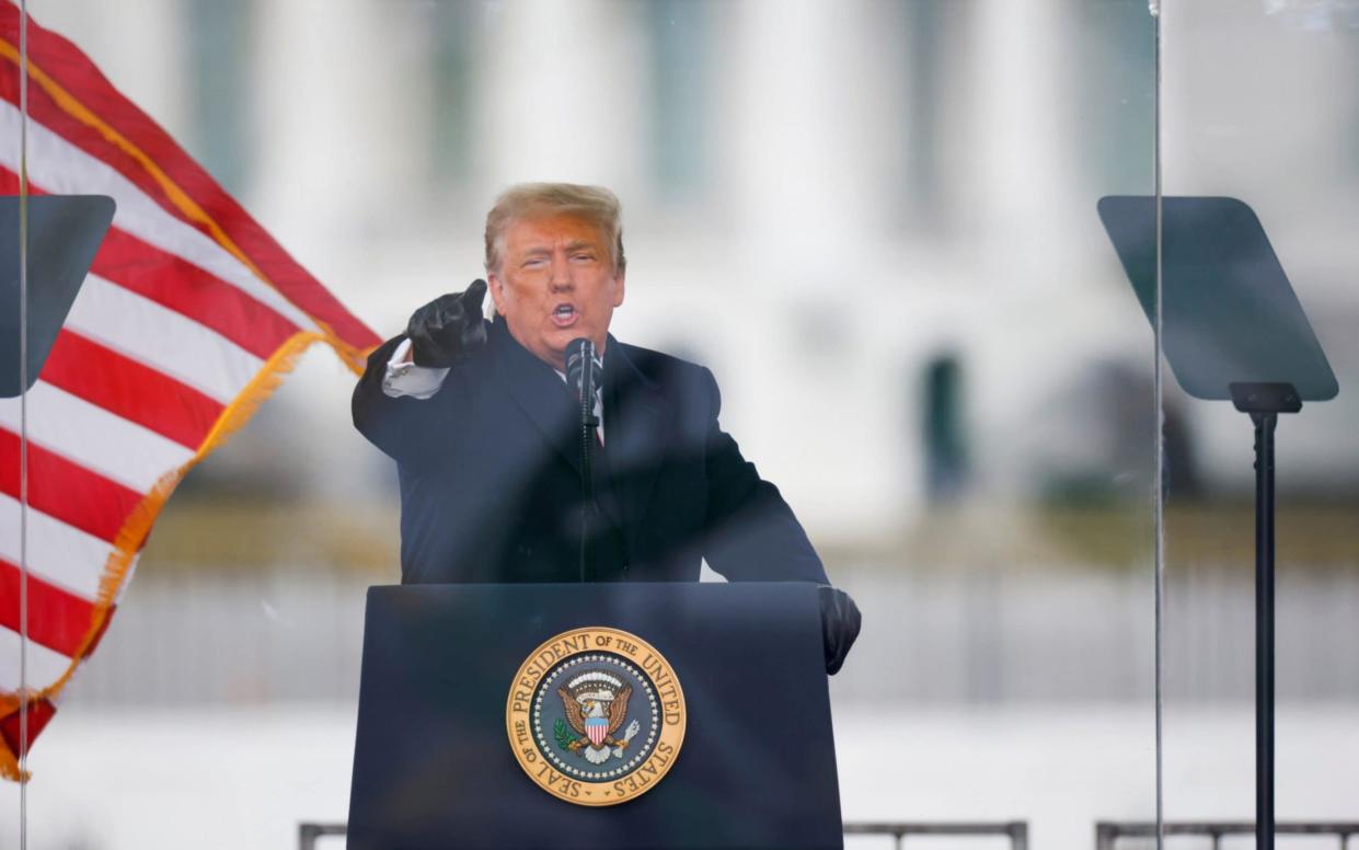 Donald Trump reaches out one black-gloved hand to point into the camera as he addresses his supporters just before the storming of the US Capitol on Jan 6. His black gloves, bulky black greatcoat and black lectern bearing the President's seal contrast sharply with his white shirt cuffs and the pillars of the White House behind him, as well as the bright red stripes of an American flag fluttering nearby. All of this is happening behind a transparent coronavirus shield, making it look as if he is speaking from inside a giant television screen, hovering eerily above the White House Lawn. - Jim Bourg/Reuters