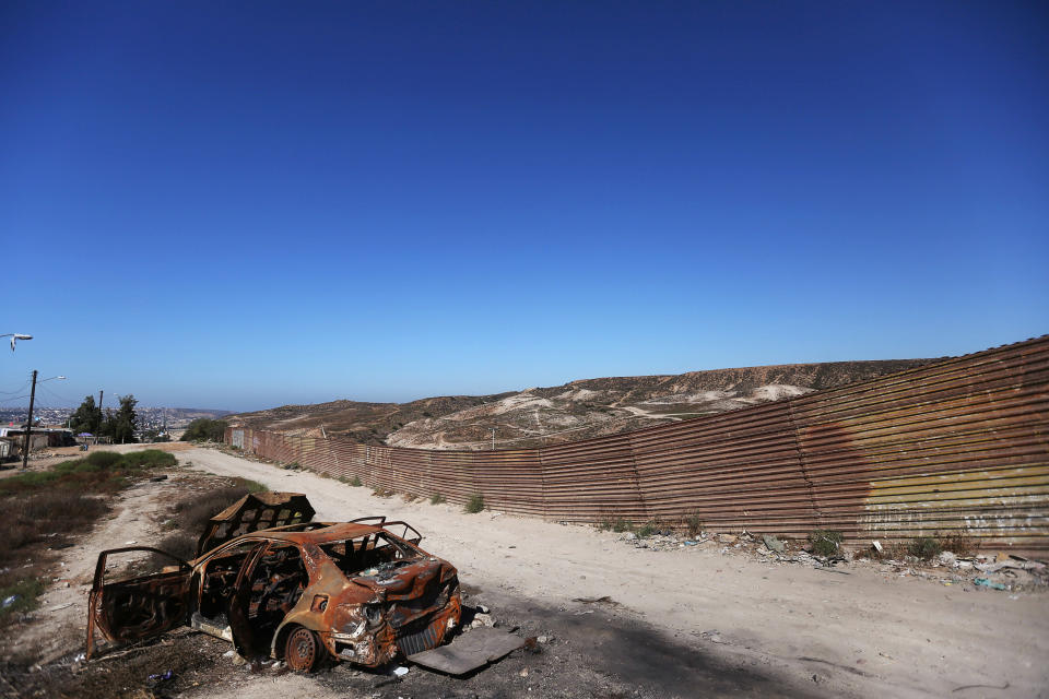 A burnt car is seen next to a section of the wall separating Mexico and the United States in Tijuana, Mexico.