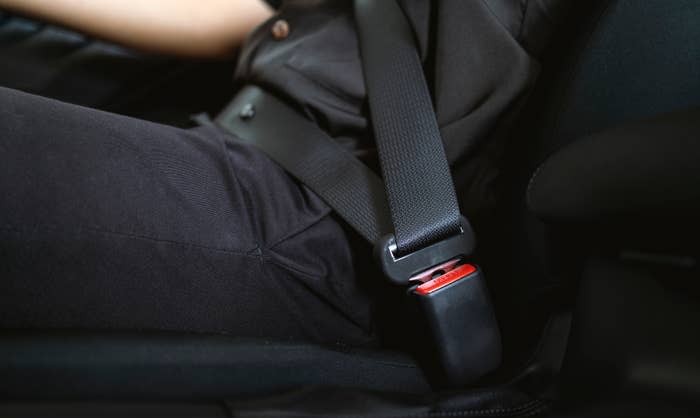 Close-up of a person wearing a seatbelt while seated in a car. Only parts of their upper torso and legs are visible