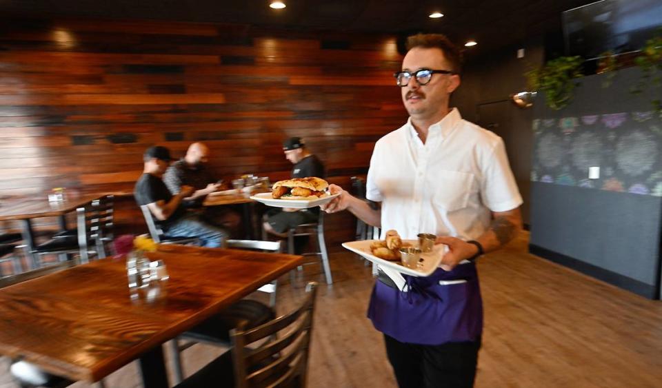 El mesero Adam Lundell lleva comida a los clientes del restaurante Cora en Roseburg Square en Modesto, California, el viernes 24 de mayo de 2024.