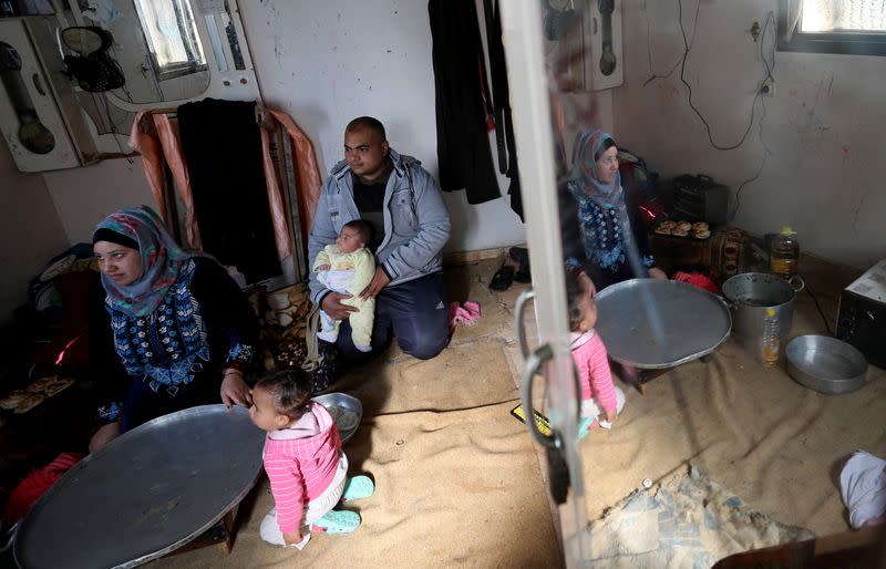 Palestinian man Eyad Al-Zahar carries his son as his wife prepares food in their home in Gaza City