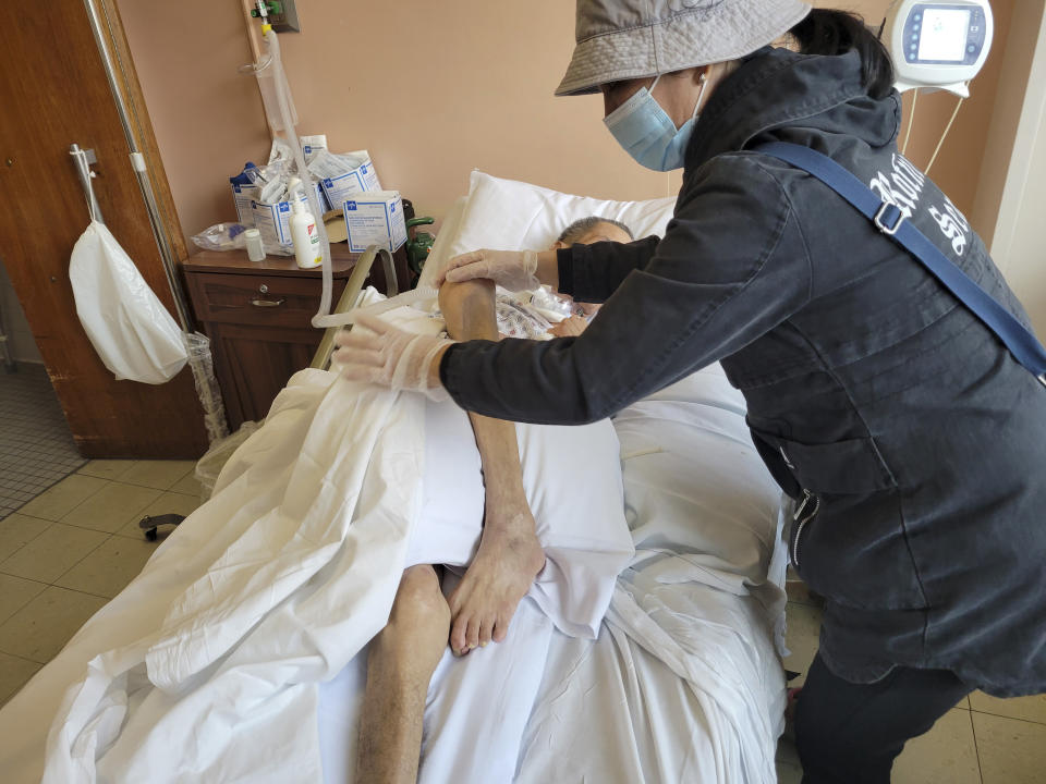 In this Wednesday, Oct. 27, 2021, photo provided by Karlin Chan, Baozhen Chen, right, assists her husband Yao Pan Ma in the hospital after he was attacked in April while collecting cans in the East Harlem neighborhood of New York. Ma, a Chinese immigrant, died Dec. 31 and his attacker, forty-nine-year-old Jarrod Powell, who was previously charged with attempted murder, felony assault and hate crimes charges, now faces a homicide charge. (Karlin Chan via AP)