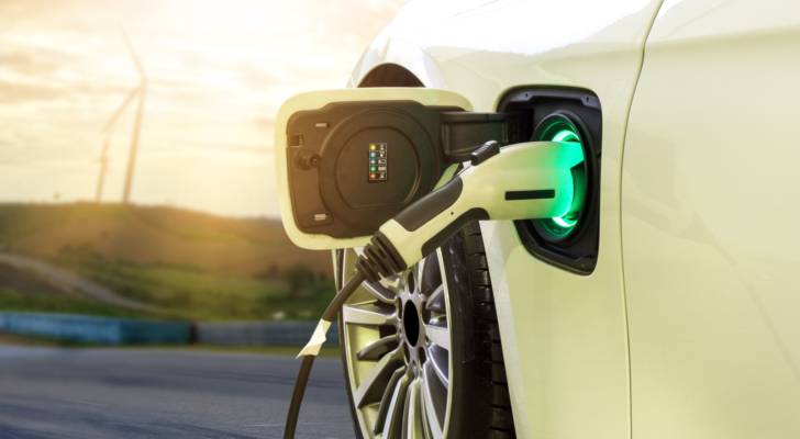 Electric car or EV car charging in station on blurred of sunset with wind turbines in front of car on background. Eco-friendly alternative energy concept. best battery stocks to buy