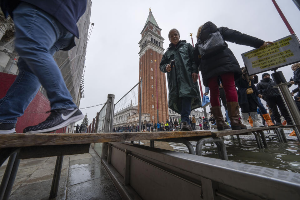 Tourists and residents walk on catwalks during a sea tide of around 97 centimeters (38.18 inches) to cross a flooded St. Mark's Square in Venice, northern Italy, Saturday, Dec. 10, 2022, where recently installed glass barriers prevent seawater from flooding the 900-year-old iconic St Mark's Basilica, left. St. Mark's Square is the lowest-laying city area and frequently ends up underwater during extreme weather. (AP Photo/Domenico Stinellis)