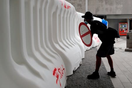 An anti-extradition bill protester peeks though barriers as he faces riot police during a march in Hong Kong