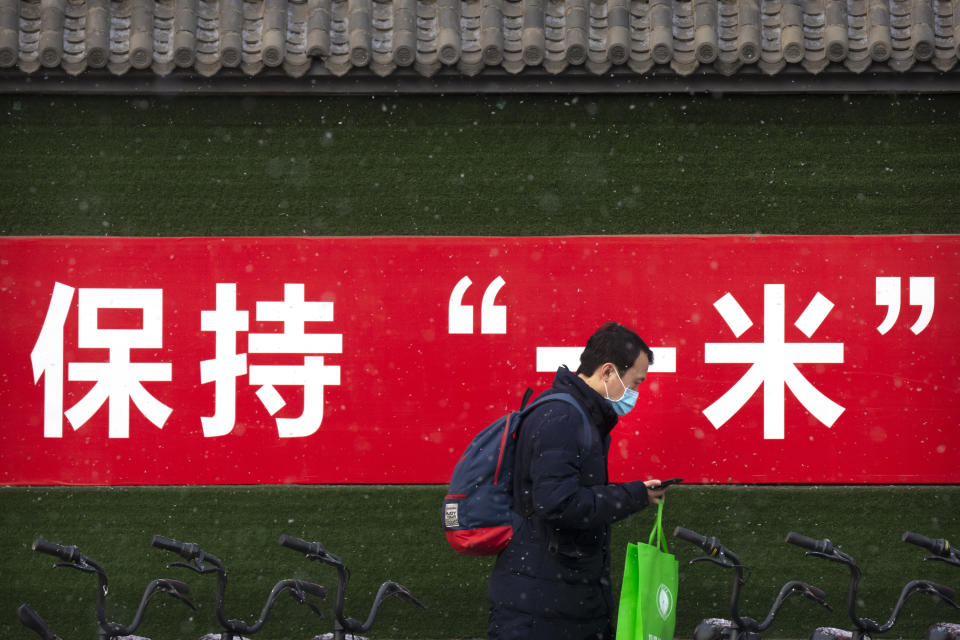 A man wearing a face mask to protect against the spread of the coronavirus walks past a billboard urging people to keep 1 meter apart for social distancing during a snowy morning in Beijing, Tuesday, Jan. 19, 2021. A Chinese province near Beijing grappling with a spike in coronavirus cases is reinstating tight restrictions on weddings, funerals and other family gatherings, threatening violators with criminal charges. (AP Photo/Mark Schiefelbein)