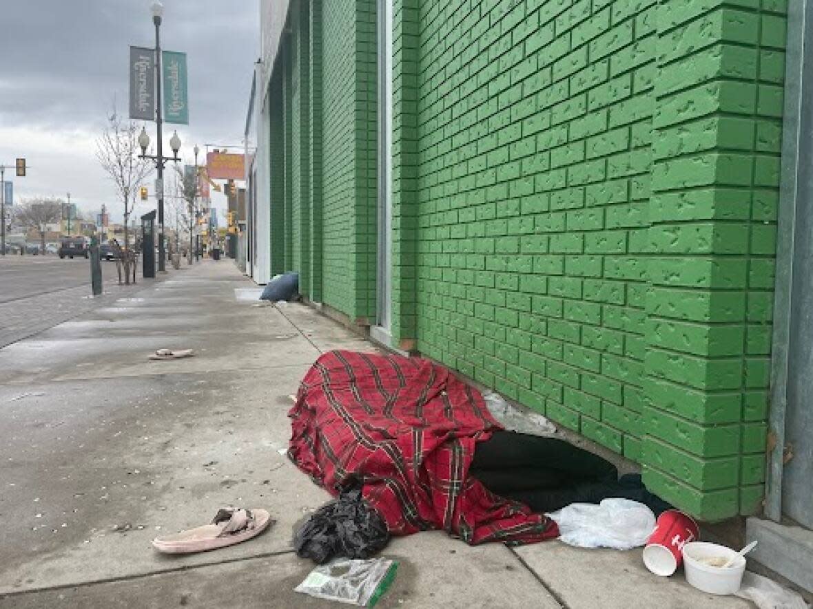 A homeless man sleeps on the street in front of the Friendship Inn in the Riversdale neighbourhood.  (Leisha Grebinski/CBC - image credit)