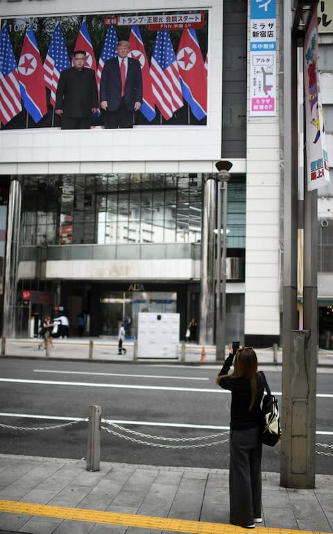 A woman takes pictures of a screen displaying live news of meeting in Tokyo - Credit: MARTIN BUREAU/AFP