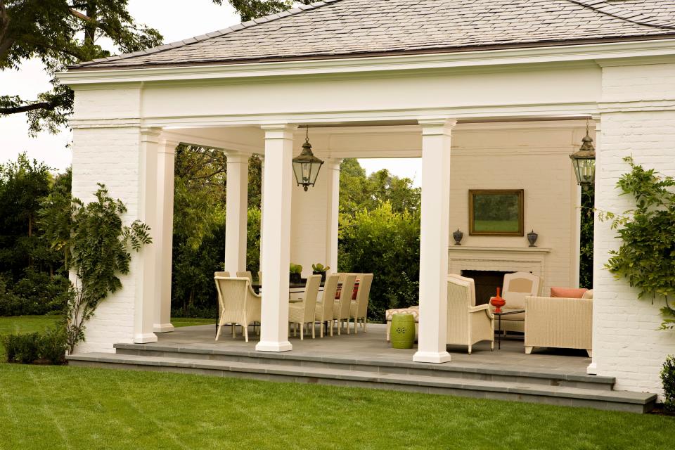 In the outdoor loggia, there’s a dialogue between the rustic texture of the white-painted brick and the refinement of the Doric architectural details. The room is roofed in gray Vermont slate. And the seating and dining areas, crowned by lanterns from Soane Britain, look out onto the lush lawn.