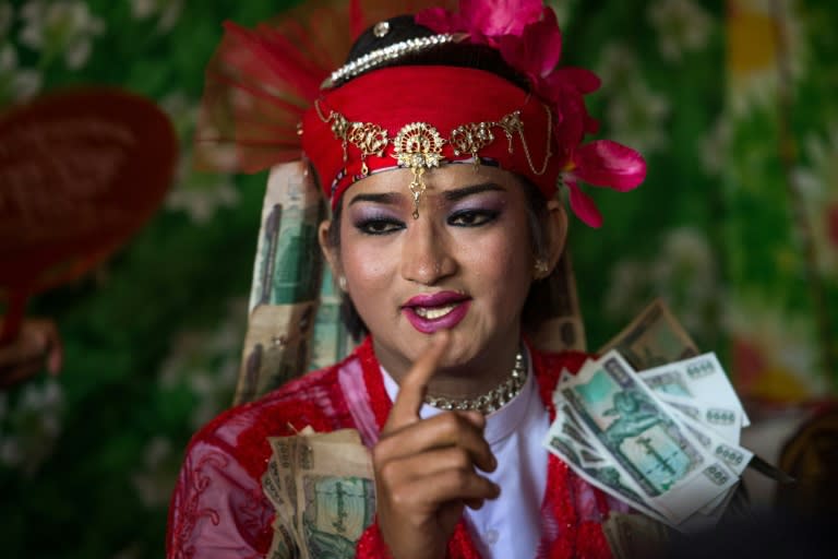 A medium wearing a red outfit and heavy make-up prepares to dance in honour of Myanmar's spirit guardian of drunkards and gamblers