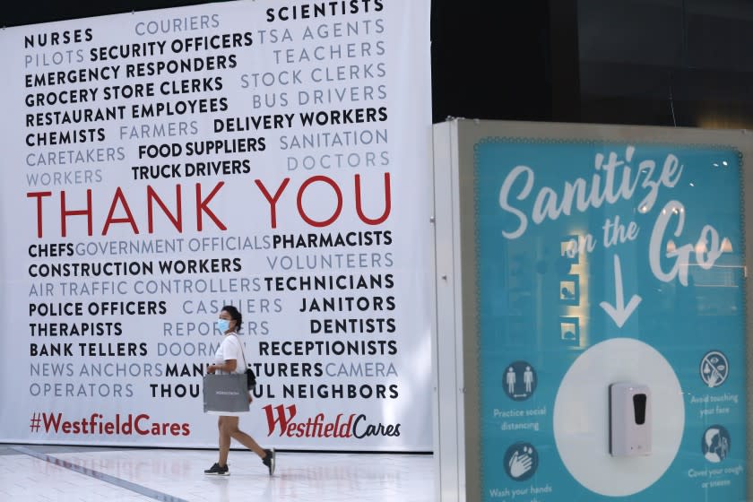 ARCADIA, CA - OCTOBER 07, 2020 - A shopper makes her way past a sign that thanks first responders that rests next to a "Sanitize on the Go," station to keep shoppers safe from coronavirus at the Westfield Santa Anita shopping mall in Arcadia on October 7, 2020. This is the first day customers return to indoor shopping after Los Angeles County eases restrictions and have reopened the malls and the individual stores. Such stores have been closed for weeks, but reopened Wednesday at 25% capacity. Westfield Santa Anita has placed Covid-related signage with one-way traffic, 6 feet distancing when waiting to get into individual stores, hand sanitizing stations and mask are required before entering the mall. (Genaro Molina / Los Angeles Times)