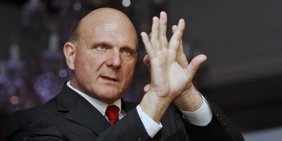 Steve Ballmer holding up his hands while wearing a black suit with a red tie.