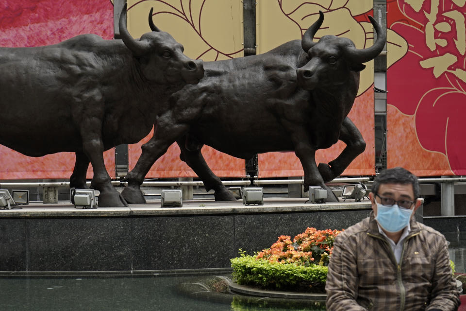 A man sits in front of the bull statues in Central, a business district in Hong Kong, Wednesday, Feb. 19, 2020. Russia says it will temporarily ban Chinese nationals from entering the country amid the outbreak of the new virus centered in China that has infected more than 73,000 people. (AP Photo/Kin Cheung)