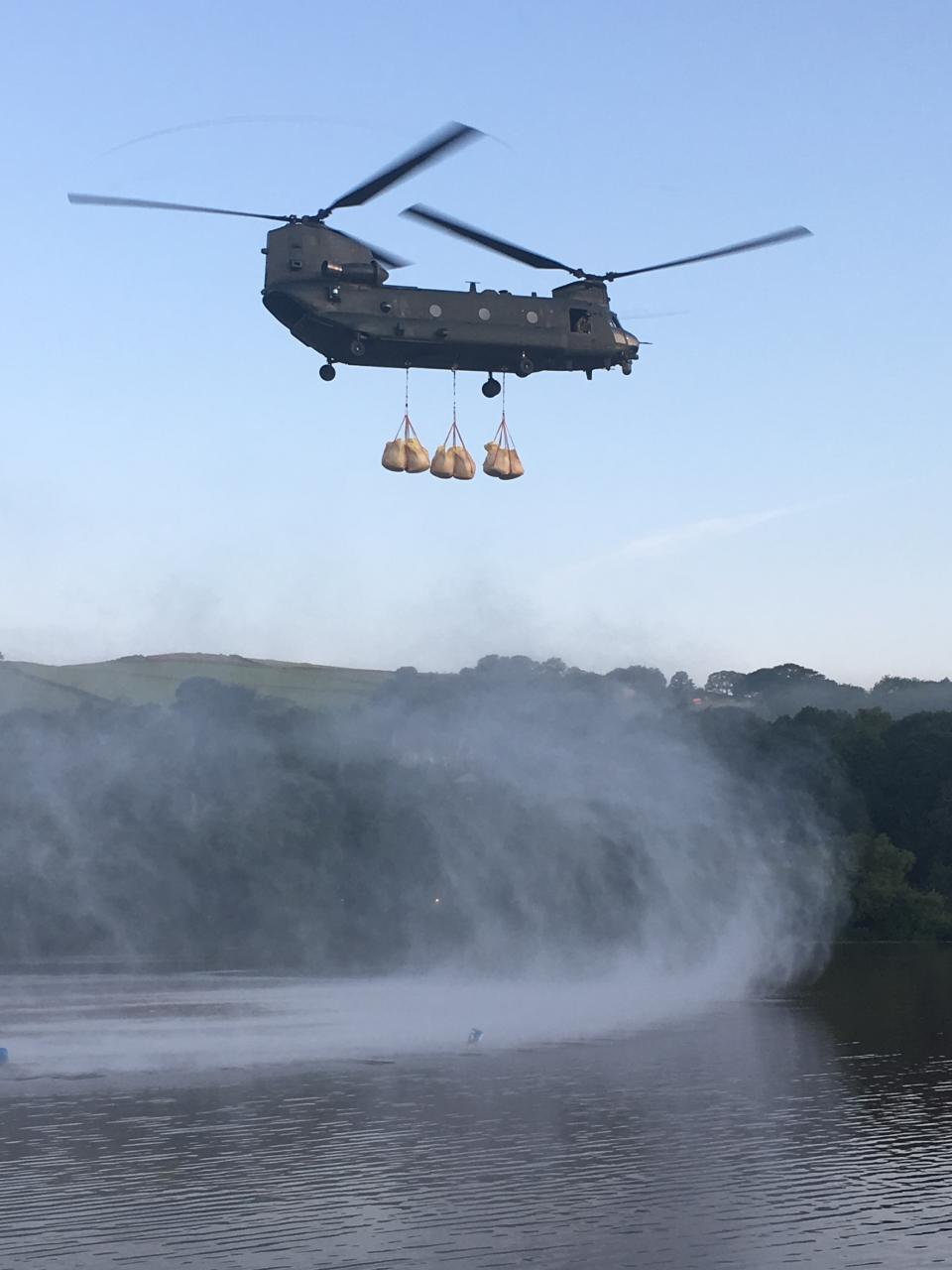 In this image released by the Ministry of Defence, an RAF Chinook helicopter flies in sandbags to help repair the dam at Toddbrook reservoir near the village of Whaley Bridge in Derbyshire, England, Friday, Aug. 2, 2019. A British military helicopter dropped sandbags Friday to shore up a reservoir wall as emergency services worked frantically to prevent a rain-damaged dam from collapsing. Engineers said they remain "very concerned" about the integrity of the 19th-century Toddbrook Reservoir, which contains around 1.3 million metric tons (1.5 million (U.S tons) of water. (Gary Lane/Ministry of Defence via AP)