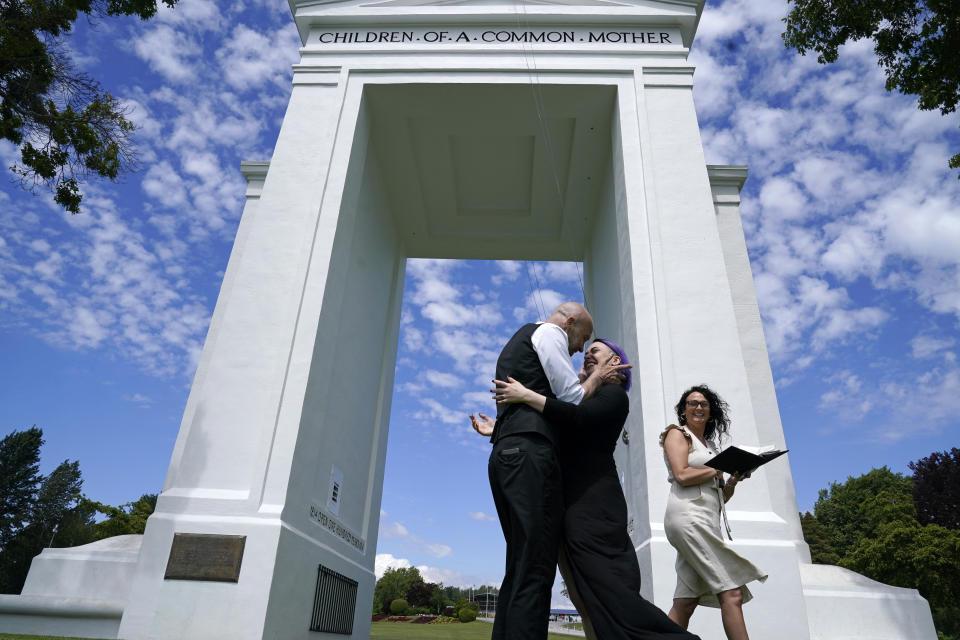 Joel Gardiner, left, embraces his new bride Mandi Gardiner as officiant Brooke Bakogeorge steps away after marrying the couple at the arch separating the U.S. from Canada at Peace Arch Historical State Park Tuesday, June 8, 2021, in Blaine, Wash. Gardiner, of Canada, walked across the border at the park into the U.S. earlier in the day to wed his American sweetheart. The border has been closed to nonessential travel since March 2020, but Canadians have been allowed to walk over a ditch into the U.S. park and weddings have become routine there. (AP Photo/Elaine Thompson)