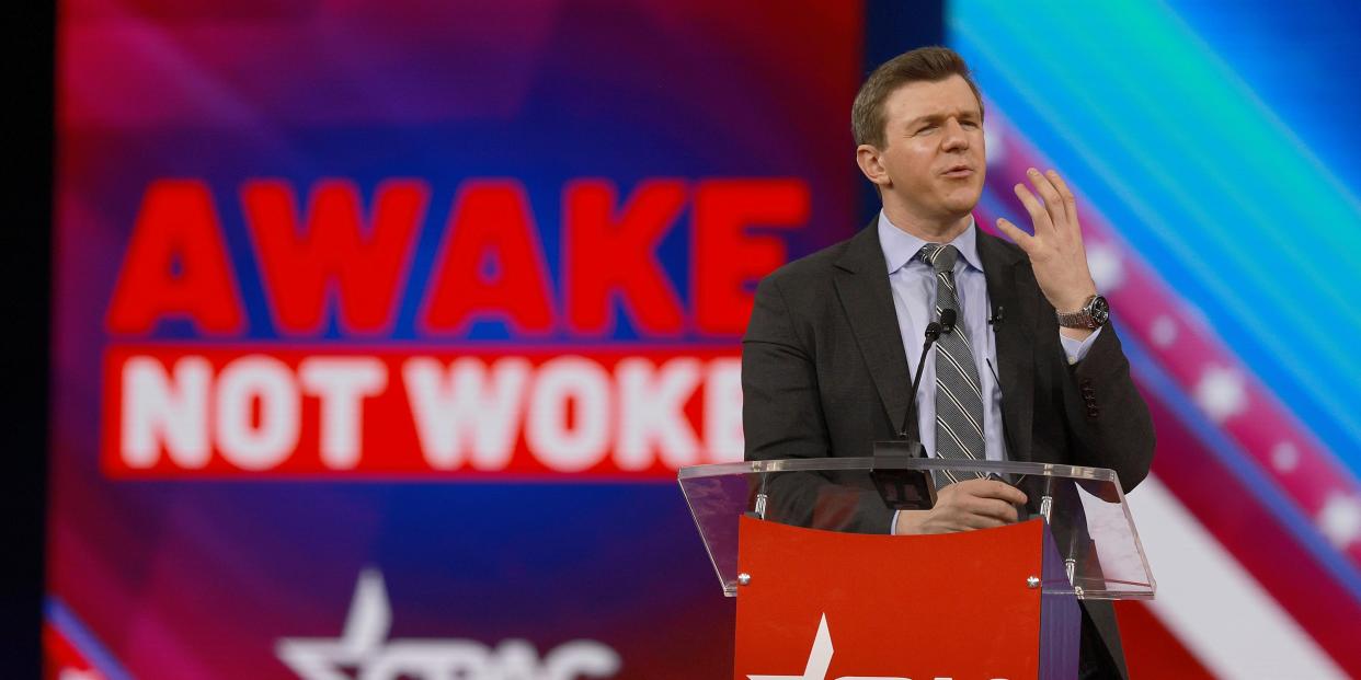 white man in suit behind podium that says "CPAC" with ghraphic behind him that says "Awake not woke"