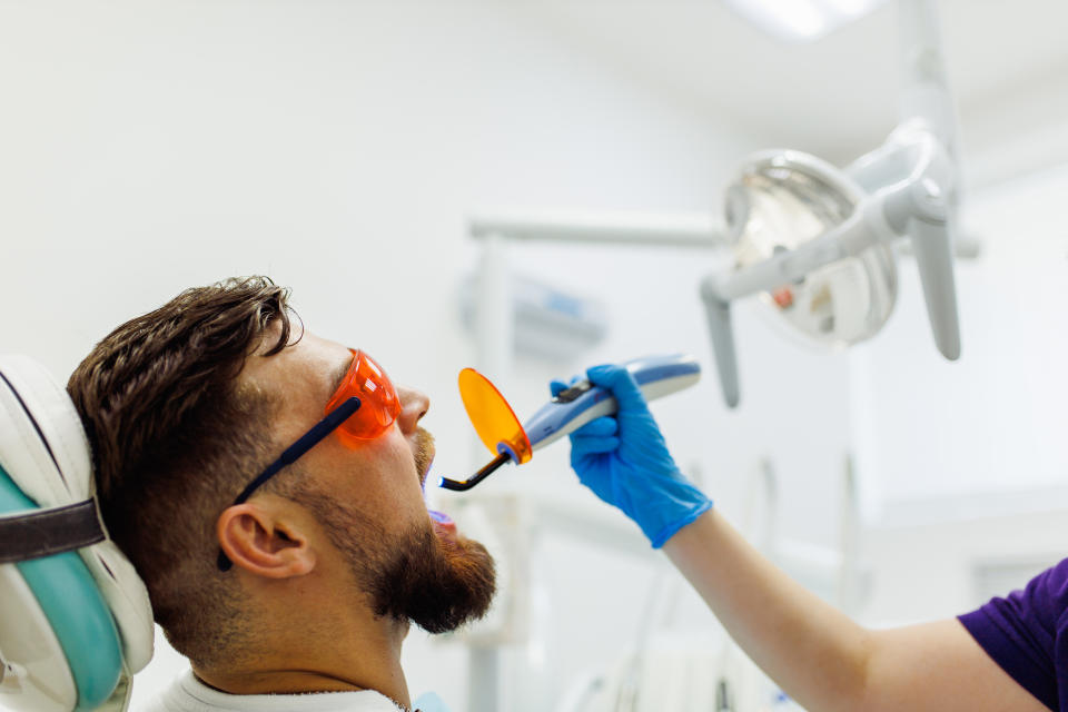 a brown haired man at the dentist while someone uses a uv light in his mouth