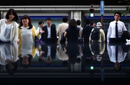 Pedestrians crossing a road in front of an electronic board showing various stock prices outside a brokerage are reflected in a polished stone surface, in Tokyo May 13, 2014. REUTERS/Yuya Shino