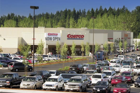 The front of a Costco warehouse with a full parking lot, and a sign reading "Now open."