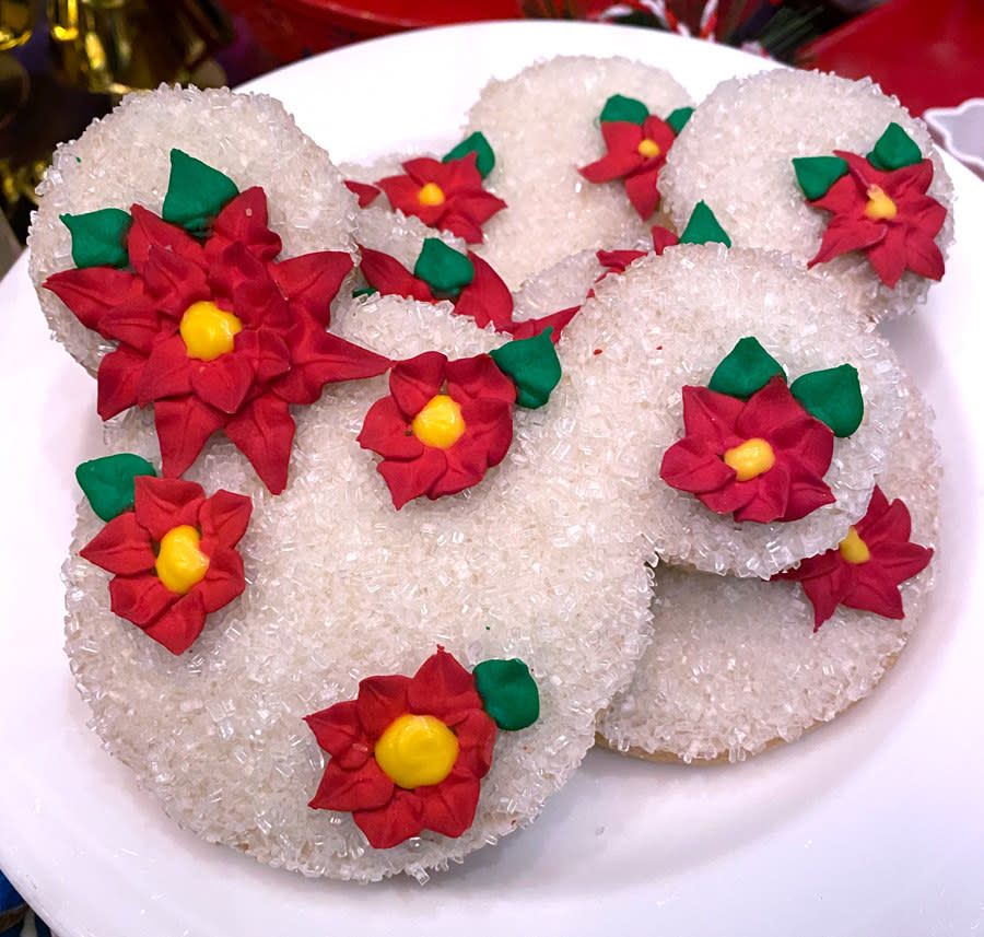Mickey shaped cookies covered in white crystal sprinkles, and poinsettia flowers made of frosting