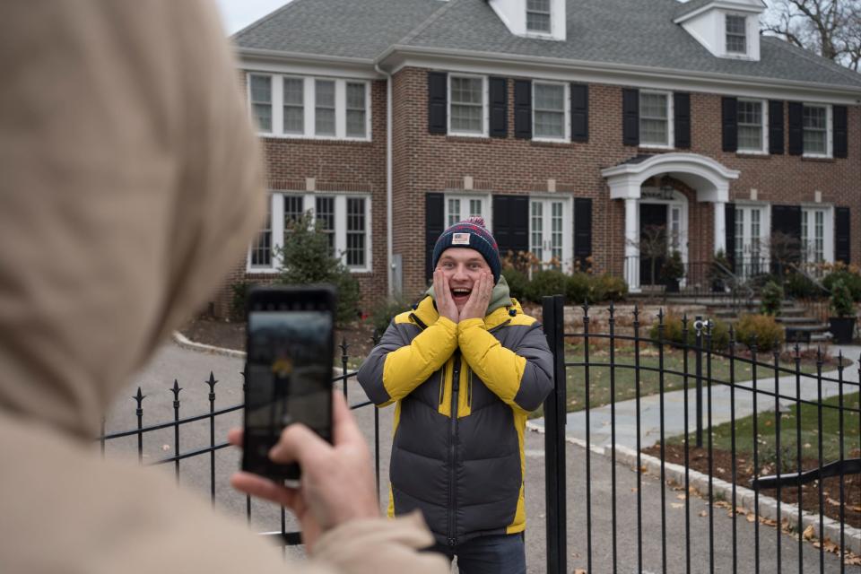 A man takes a photo in front of a red brick home