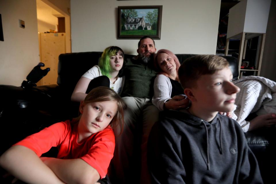 James Hogan II sits with his wife, Rebekah, daughter Caleigh, 15, and sons Sebastian, 9, and Ben, 14, in the living room of their home in Latham, N.Y. April 7, 2022. In October 2020, the entire family contracted COVID-19. Almost a year and a half later, they all suffer symptoms of long COVID. James, a disabled military veteran is on permanent disability, and has had to take on the role of caregiver for his family despite his lingering symptoms. Rebekah, a registered nurse, has been unable to work due to her COVID symptoms. As a result the family has eaten into much of their life savings.