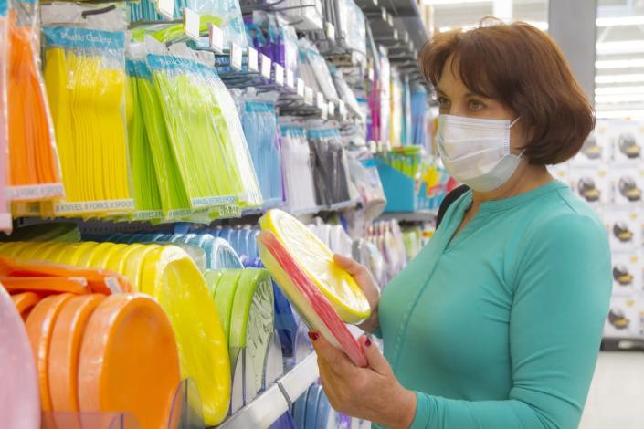 Close portrait of happiness latin mature woman choosing and shopping plastic cutlery for a party in a megastore in United States, wearing a light blue shirt and face mask standing in front of the display in the department store some days before holidays.