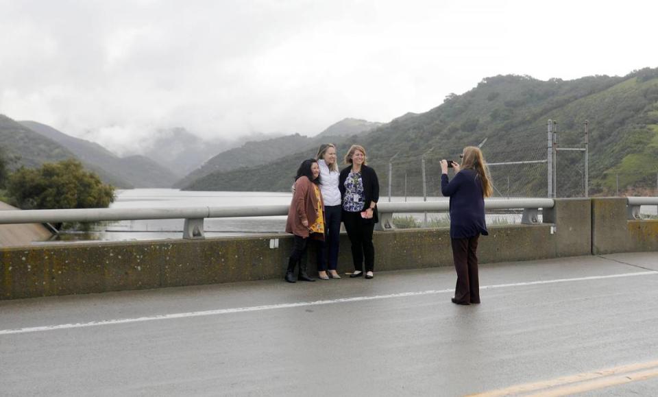 A group of women take photos on top of the lake dam and spillway. Lake Lopez finally naturally spills over the chute in the early morning, Thursday, Mar. 23, 2023.