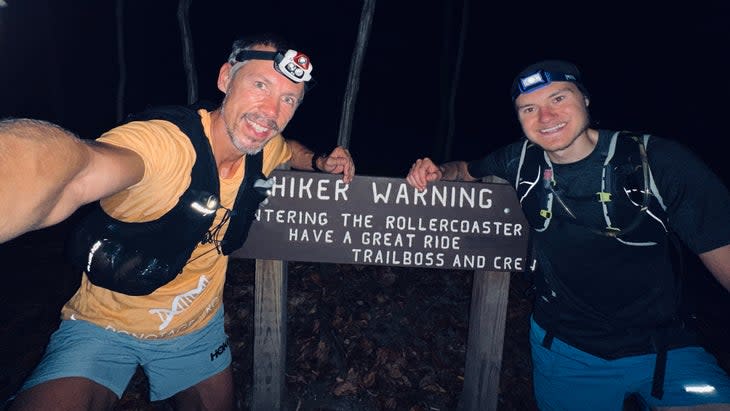 A man and a friend are hiking at night with a sign