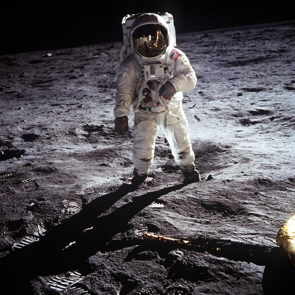 Astronaut in spacesuit standing on the moon's surface with visor reflecting the lunar module