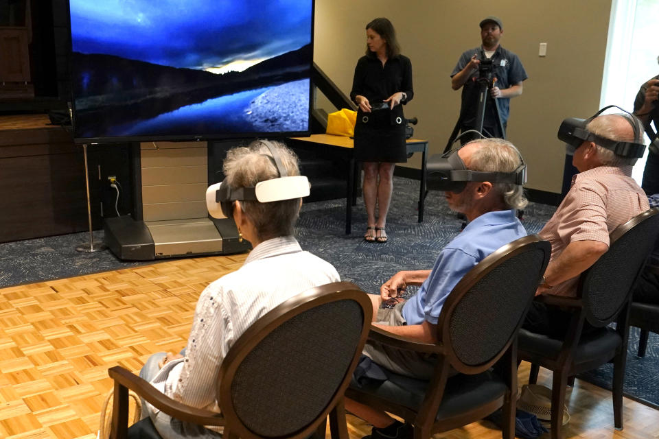 Residents of John Knox Village wear goggles as a virtual reality image is projected on a screen, Tuesday, June 1, 2021, in Pompano Beach, Fla. The senior community is in partnership with Stanford University's Virtual Human Interaction Lab on a study to see how older adults respond to virtual reality and whether it can improve their sense of wellbeing. (AP Photo/Lynne Sladky)