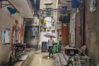 A woman, wearing a face mask, walks through residential buildings as cleaning worker moves a trash bin in Guangzhou's Xiaobei neighborhood