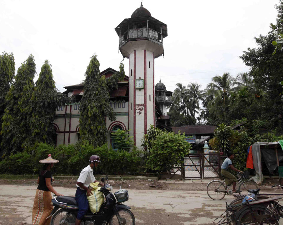 A couple carries goods on their motorbike as a man rides a bicycle on a road by a mosque Wednesday, Oct. 2, 2013, in Thandwe, Rakhine State, western Myanmar. Terrified Muslim families hid in forests in western Myanmar on Wednesday, one day after rampaging Buddhist mobs killed a 94-year-old woman and burned dozens of homes despite the first trip to the volatile region by President Thein Sein since unrest erupted last year. The violence near Thandwe, a coastal town the president was due to visit later Wednesday on the second day of his tour of Rakhine state, raised new questions about government's failure to curb anti-Muslim attacks and or protect the embattled minority. (AP Photo/Khin Maung Win)