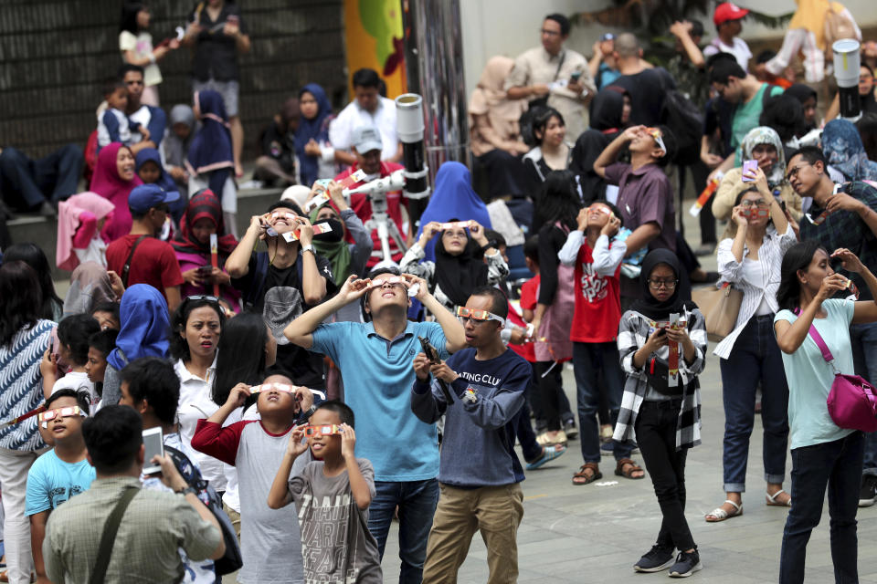 People look up at the sun with protective glasses to watch a solar eclipse from Jakarta, Indonesia, Thursday, Dec. 26, 2019. (AP Photo/Tatan Syuflana)