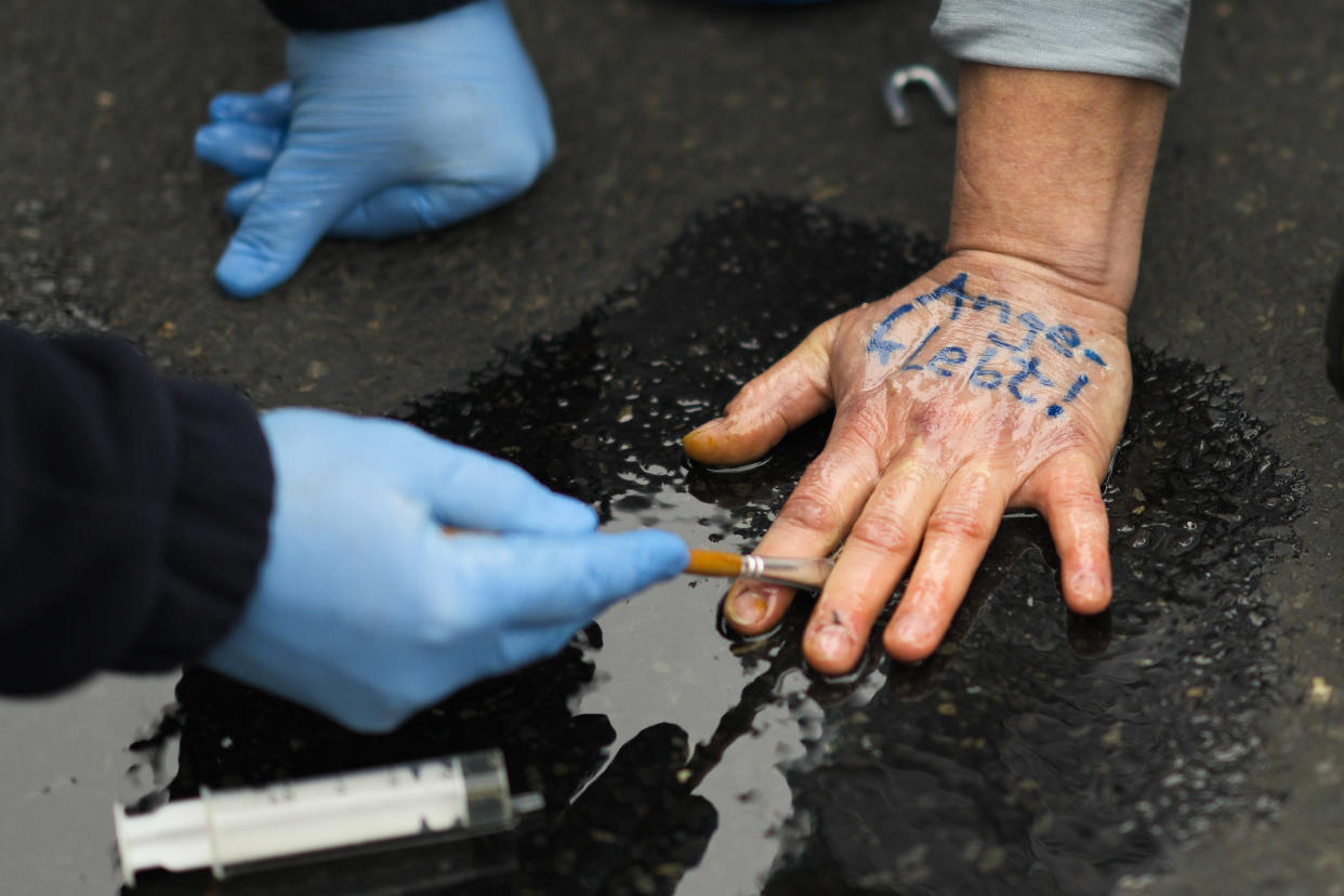 FILE - A police officer removes glue from the hand of a climate protester who attached himself to a road, during a protest in Berlin, Germany, April 6, 2022. The climate change generation is saying officials are talking too much, listening too little and acting even less. And they are fed up. (AP Photo/Markus Schreiber, File)